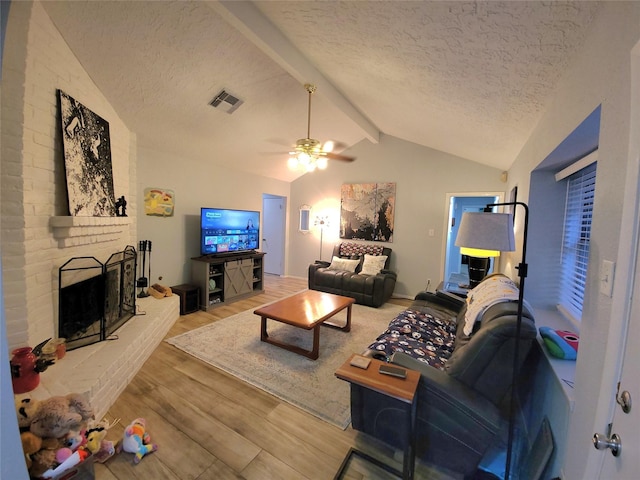 living room with lofted ceiling with beams, a textured ceiling, a brick fireplace, and wood finished floors