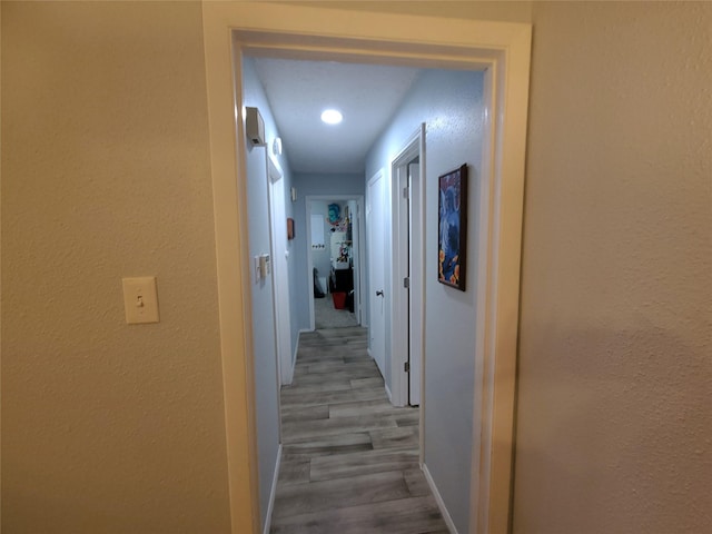 hallway featuring a textured wall, baseboards, and wood finished floors