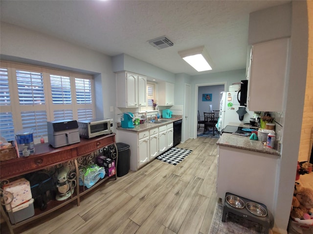 kitchen with light wood-style floors, stainless steel microwave, black dishwasher, and white cabinets