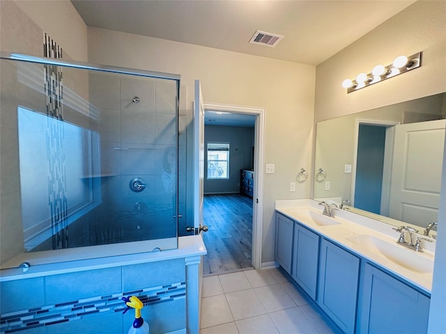 full bathroom with a tile shower, double vanity, a sink, and visible vents