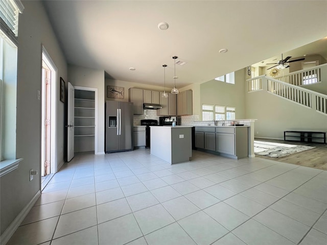 kitchen featuring a center island, light tile patterned floors, gray cabinetry, stainless steel fridge, and under cabinet range hood