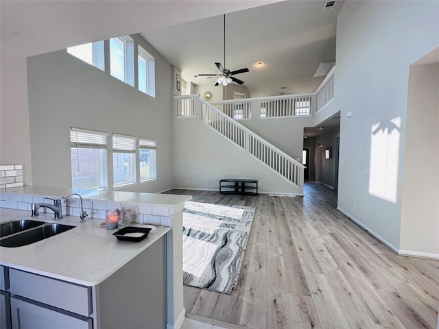 living room with baseboards, a towering ceiling, light wood-style flooring, ceiling fan, and stairs