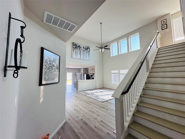 stairs featuring ceiling fan, a high ceiling, wood finished floors, visible vents, and baseboards