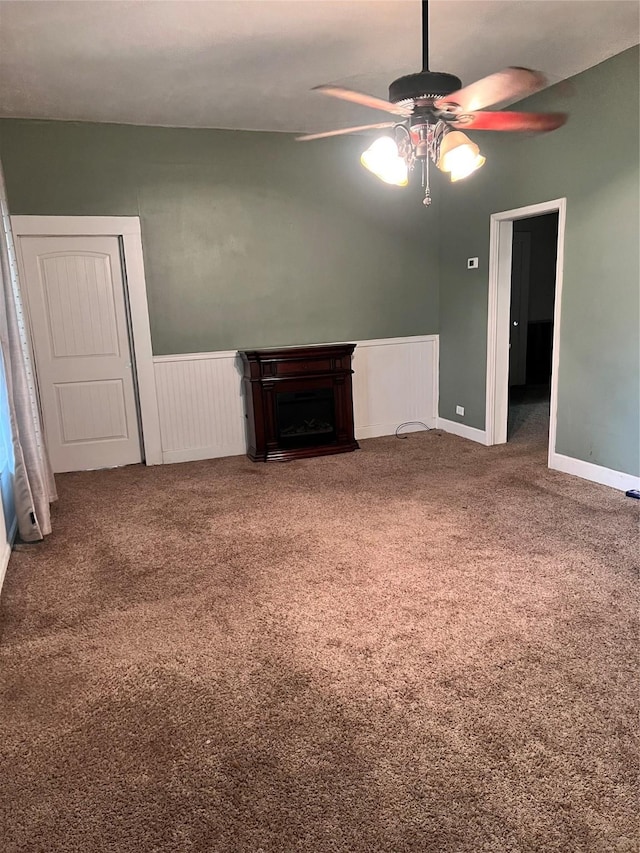 unfurnished living room with a wainscoted wall, a fireplace, a ceiling fan, and carpet flooring