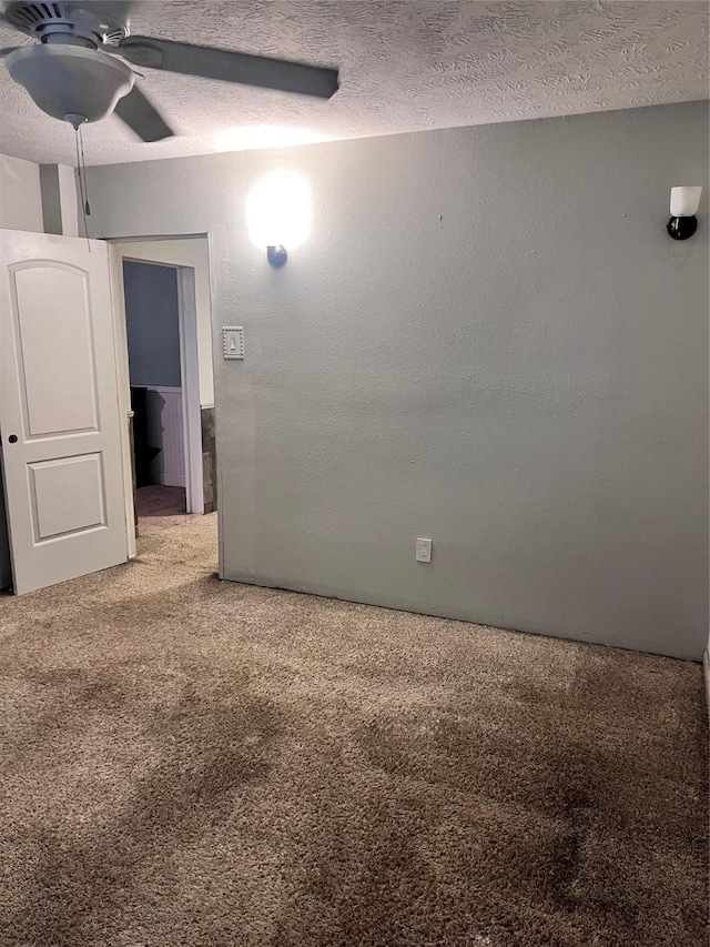 carpeted spare room featuring a textured ceiling, a textured wall, and ceiling fan