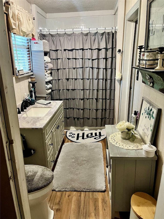 full bath with a textured ceiling, toilet, a shower with shower curtain, wood finished floors, and vanity