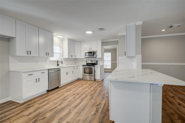 kitchen with a peninsula, a sink, white cabinetry, appliances with stainless steel finishes, and light wood finished floors