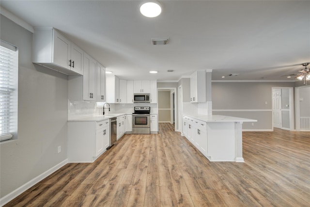 kitchen with appliances with stainless steel finishes, visible vents, a peninsula, and tasteful backsplash