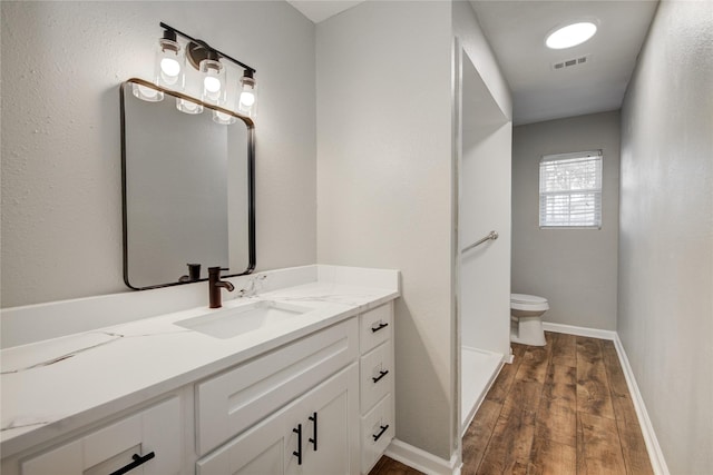 bathroom featuring visible vents, toilet, vanity, wood finished floors, and baseboards