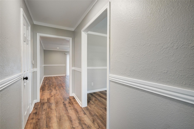 hallway with a textured wall, a wainscoted wall, crown molding, and wood finished floors