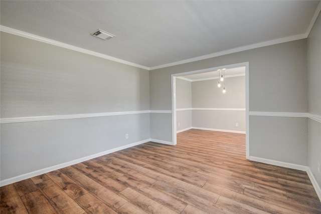 empty room with visible vents, crown molding, baseboards, and wood finished floors