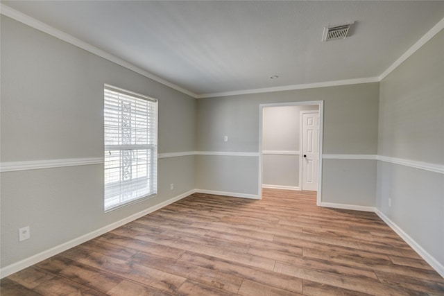 empty room featuring crown molding, wood finished floors, visible vents, and baseboards