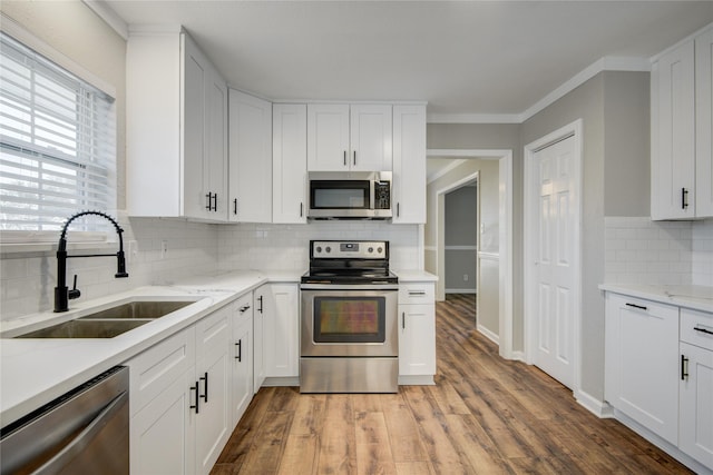 kitchen with light wood-style flooring, a sink, white cabinets, appliances with stainless steel finishes, and light stone countertops