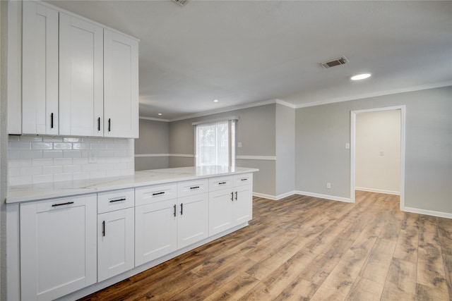 kitchen featuring tasteful backsplash, baseboards, visible vents, white cabinets, and wood finished floors