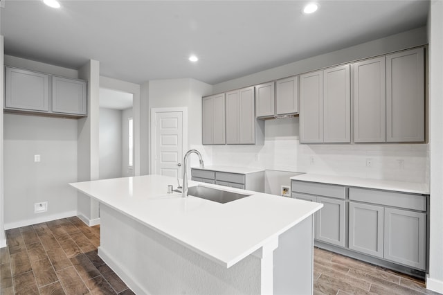 kitchen featuring a kitchen island with sink, gray cabinetry, a sink, wood tiled floor, and tasteful backsplash