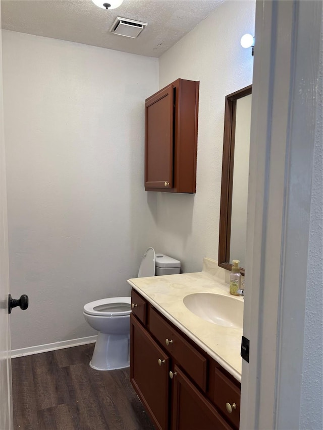 half bath featuring a textured ceiling, toilet, wood finished floors, vanity, and visible vents