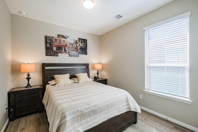 bedroom with wood finished floors, visible vents, and baseboards