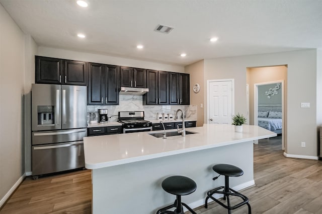 kitchen featuring a breakfast bar area, visible vents, a sink, decorative backsplash, and stainless steel appliances