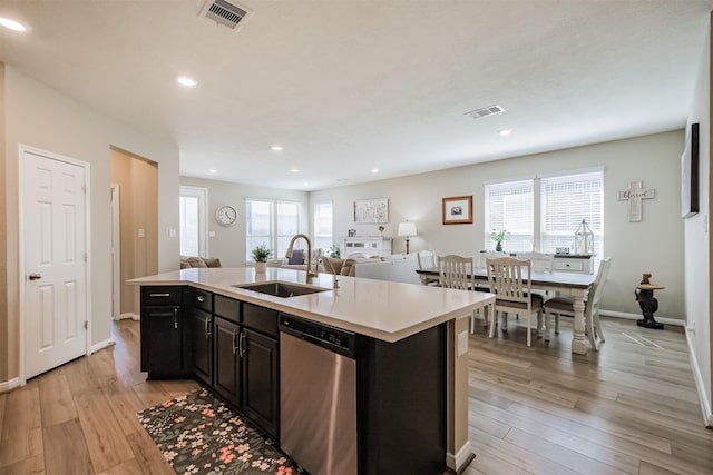 kitchen with stainless steel dishwasher, a sink, light wood-style floors, light countertops, and open floor plan