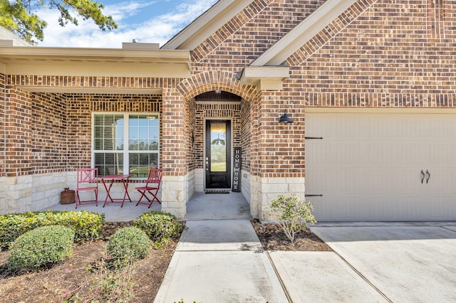 doorway to property featuring driveway, brick siding, a porch, and an attached garage