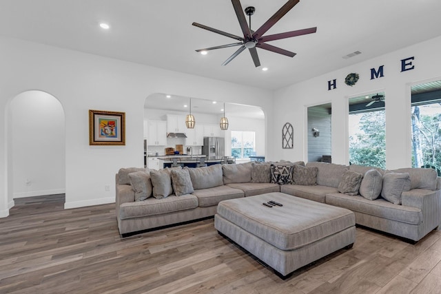 living room with arched walkways, visible vents, recessed lighting, and wood finished floors