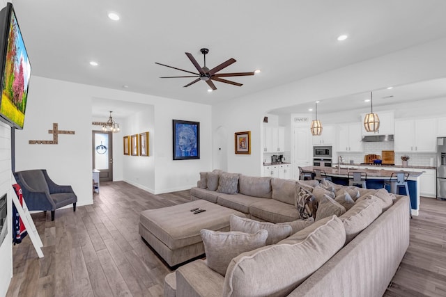 living room featuring ceiling fan with notable chandelier, baseboards, wood finished floors, and recessed lighting