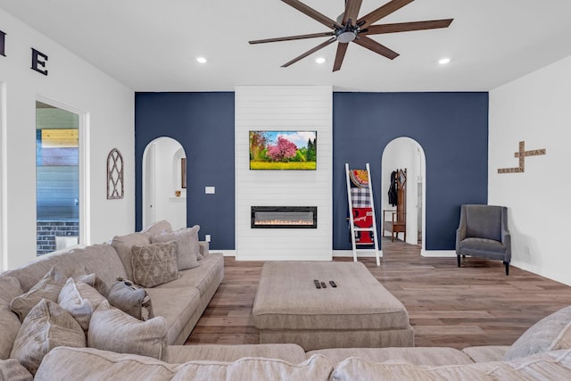 living area with arched walkways, recessed lighting, a large fireplace, wood finished floors, and baseboards