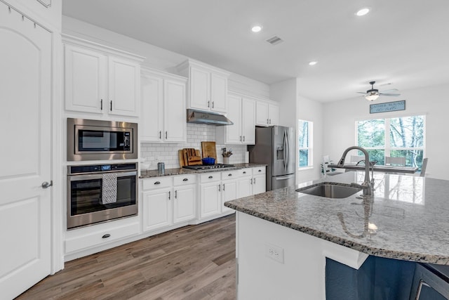 kitchen featuring appliances with stainless steel finishes, white cabinetry, a sink, dark stone counters, and under cabinet range hood