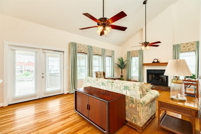 living area featuring a fireplace with raised hearth, a ceiling fan, french doors, light wood-style floors, and high vaulted ceiling