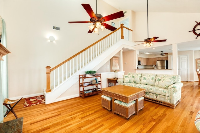 living area with visible vents, a towering ceiling, stairs, baseboards, and light wood finished floors