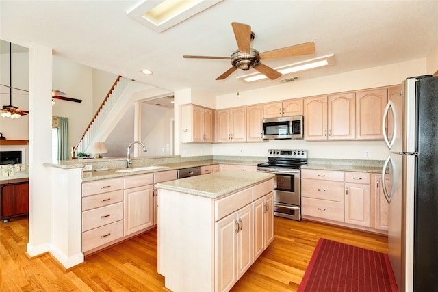 kitchen with light wood finished floors, appliances with stainless steel finishes, a sink, and light brown cabinetry