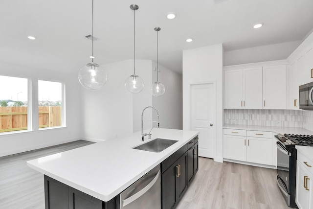 kitchen with stainless steel appliances, a sink, light countertops, decorative backsplash, and a center island with sink