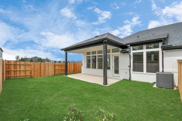 rear view of house with central air condition unit, a fenced backyard, a lawn, and a patio