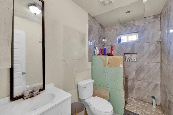 bathroom featuring visible vents, tiled shower, vanity, and toilet