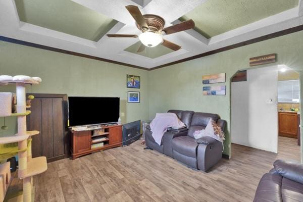 living room featuring arched walkways, a ceiling fan, ornamental molding, a tray ceiling, and light wood-style floors