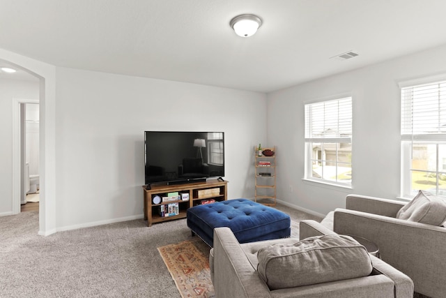 carpeted living area featuring arched walkways, visible vents, plenty of natural light, and baseboards