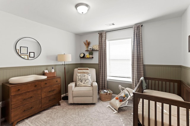 bedroom with a nursery area, visible vents, carpet flooring, and wainscoting