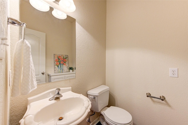 bathroom featuring toilet, a sink, and a textured wall