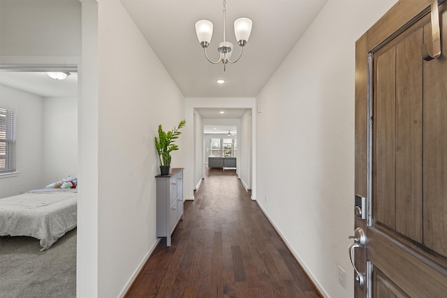 hall featuring dark wood-style floors, baseboards, and a notable chandelier