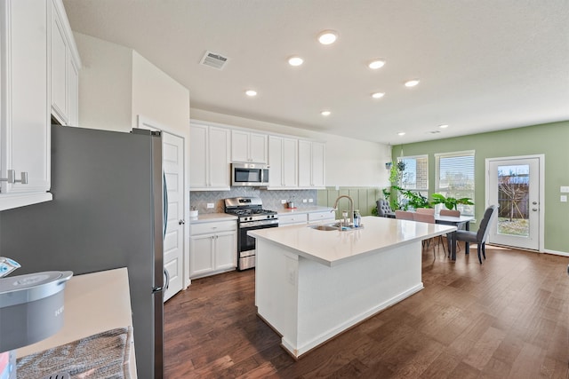 kitchen featuring dark wood-style floors, stainless steel appliances, visible vents, decorative backsplash, and a sink