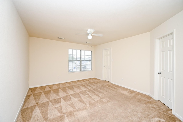 spare room featuring light colored carpet, ceiling fan, visible vents, and baseboards