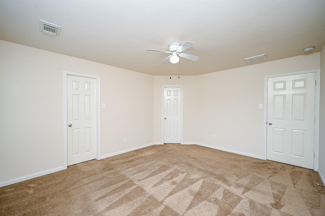 carpeted spare room with baseboards, visible vents, and ceiling fan