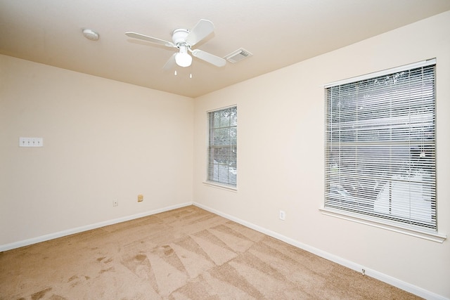 spare room featuring light colored carpet, ceiling fan, visible vents, and baseboards