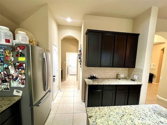 kitchen featuring arched walkways, light tile patterned floors, freestanding refrigerator, and decorative backsplash