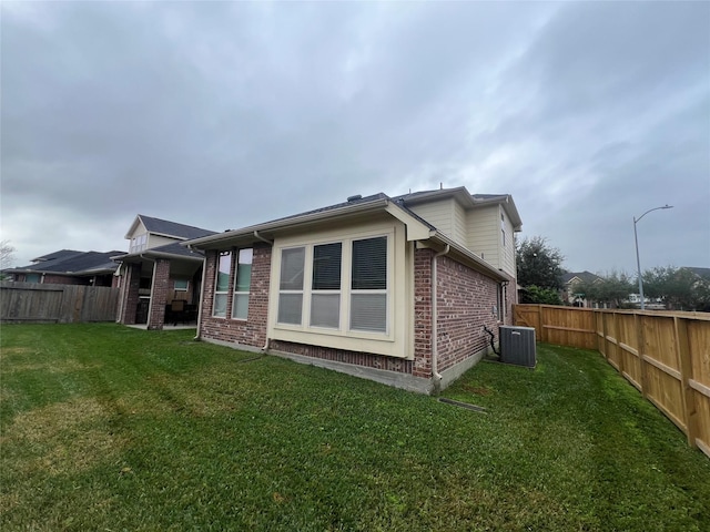 rear view of property with a yard, brick siding, a fenced backyard, and cooling unit