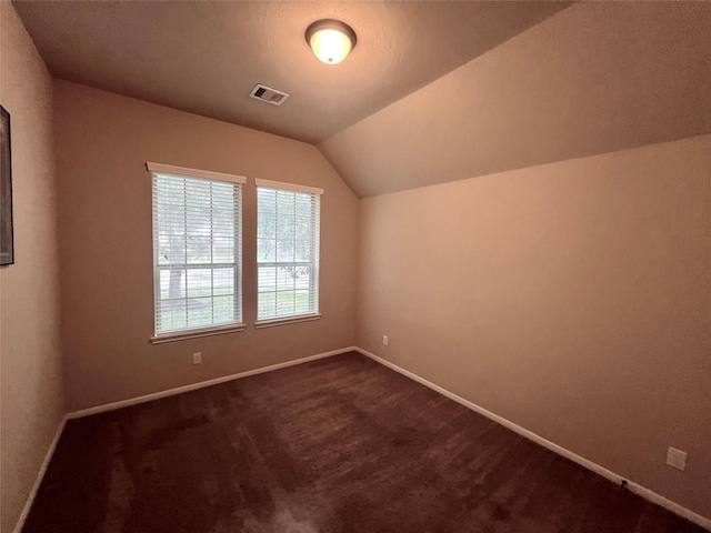 additional living space featuring vaulted ceiling, dark colored carpet, visible vents, and baseboards