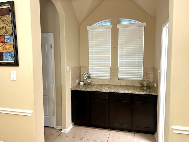 bar with light tile patterned floors, tasteful backsplash, arched walkways, and lofted ceiling