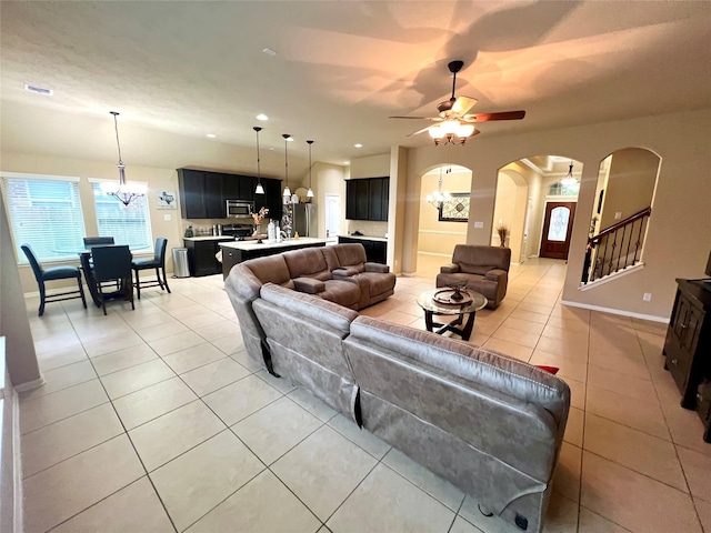 living area featuring arched walkways, recessed lighting, stairway, light tile patterned flooring, and ceiling fan with notable chandelier