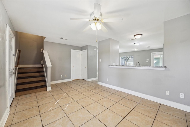 empty room featuring stairs, baseboards, a ceiling fan, and light tile patterned flooring