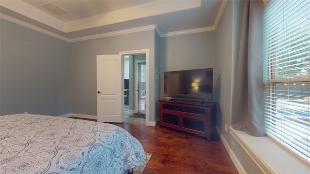 bedroom with wood finished floors, visible vents, baseboards, a raised ceiling, and crown molding